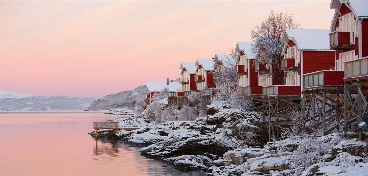 Röda stugor på pålar på de snötäckta klipphällarna i rosa vintersolnedgång