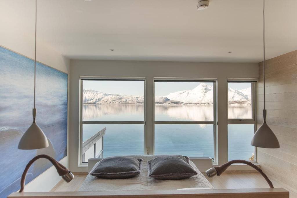 Premiumdubbelrum med sängen vänd mot fönster med utsikt över den vintriga fjorden och snötäckta fjäll