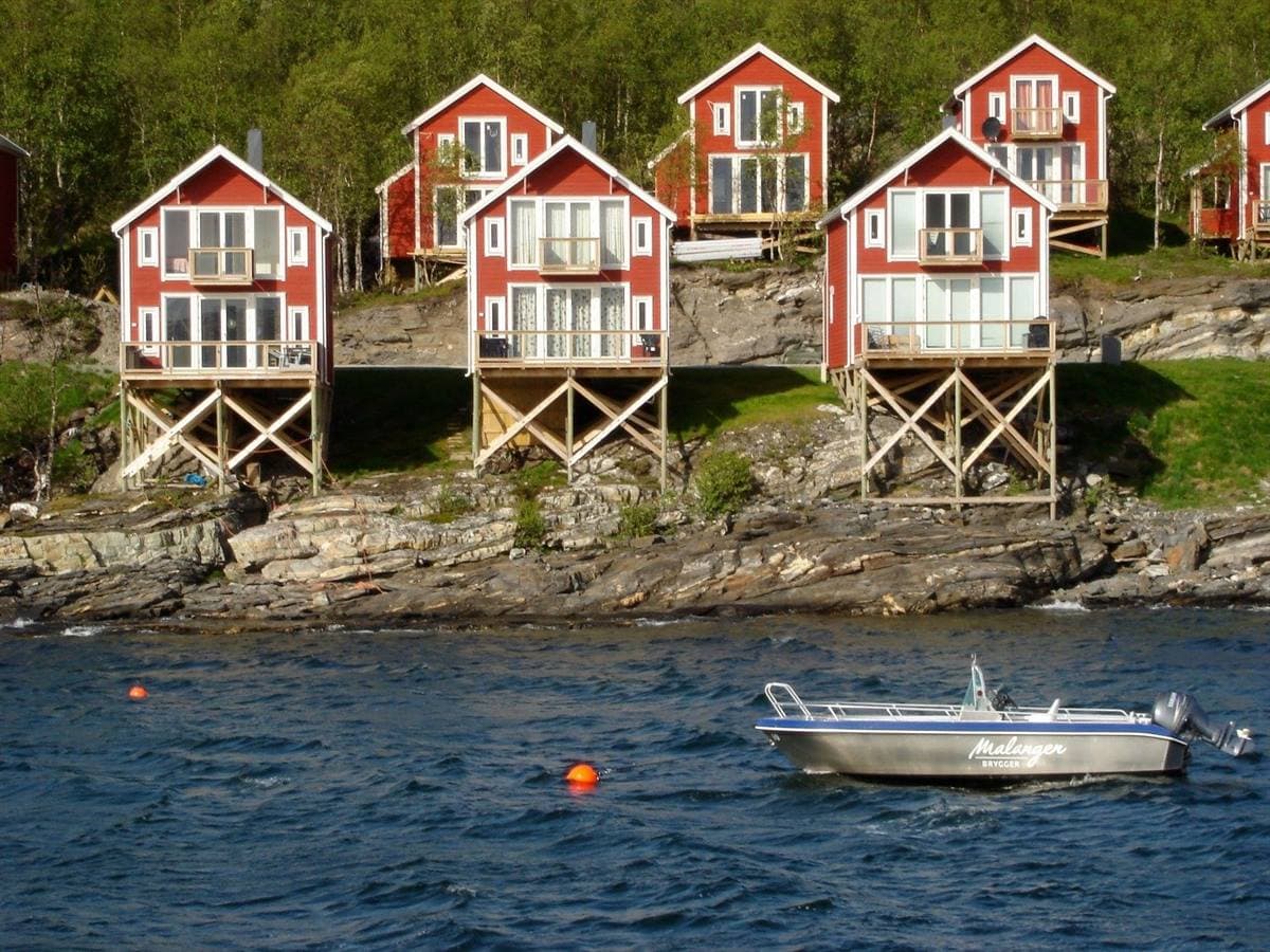 Röda stugor på pålar sedda från fjorden, med en båt framför