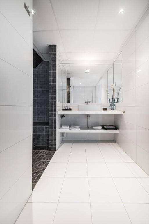 Ljust hotellbadrum med vitt kakel och walk-in-dusch