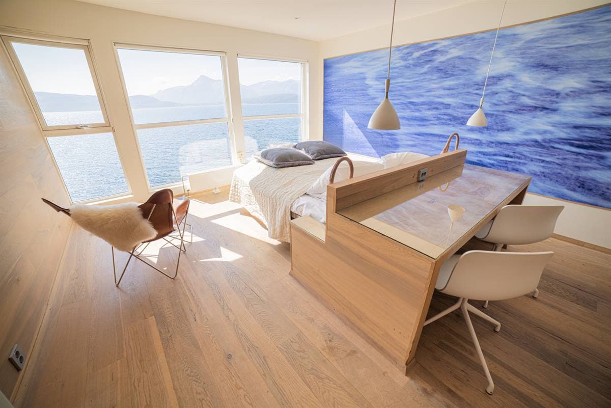 Skrivbord och säng under en väggmålning med vågor, med fönster mot fjorden