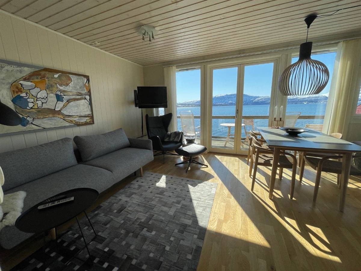Vardagsrum och matplats i lägenheten med fjordutsikt genom balkongdörrarna